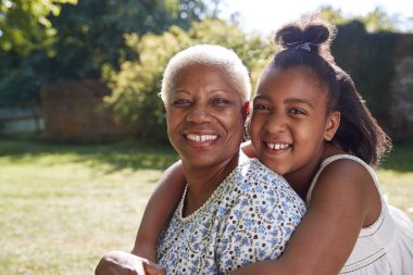 Senior black woman and granddaughter sit embracing outside clipart