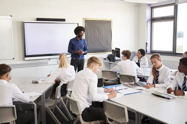 インタラクティブ ホワイト ボードの横に男性高校教師立ってと制服を着て生徒にレッスンを教える — ストック写真