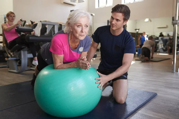 Senior Vrouw Uitoefenen Swiss Bal Gestimuleerd Door Personal Trainer Sportschool — Stockfoto