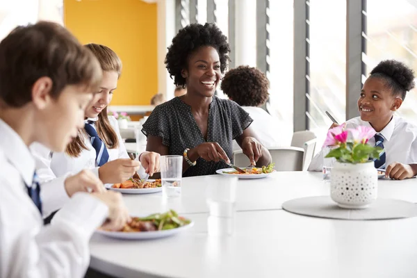 女教师与一群高中生穿着制服围坐在桌旁 在自助餐厅吃午饭 — 图库照片