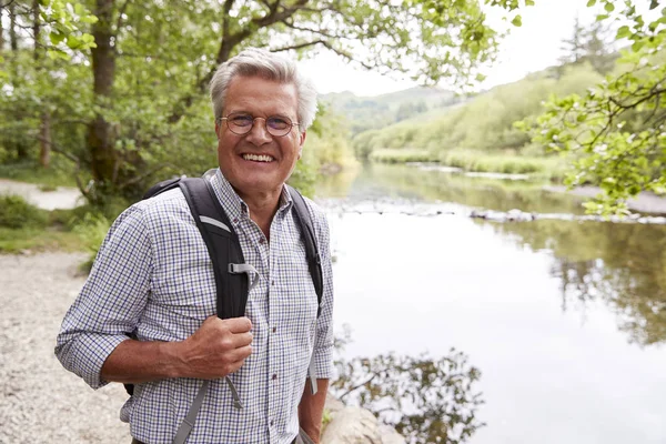 Portrait Of Senior Man Hiking Along Path By River In UK Lake District