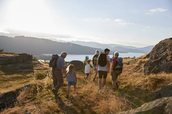 湖水地方の田園地帯をハイキングで丘の上を歩く世代家族の背面図 — ストック写真