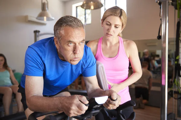 Senior Man Uitoefenen Fietsen Machine Gestimuleerd Door Vrouwelijke Personal Trainer — Stockfoto