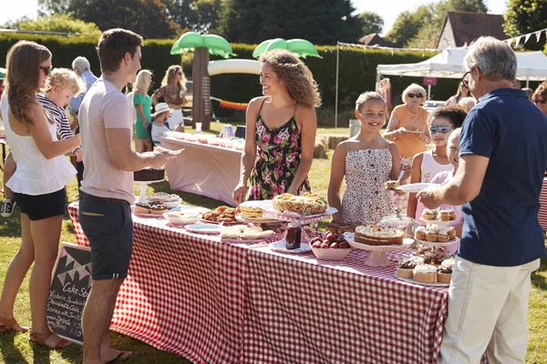 table with sweet cakes and desserts in backyard picnic, people enjoying food