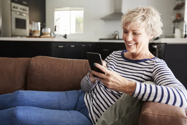 坐在家里沙发上的白人老年妇女使用智能手机 — 图库照片