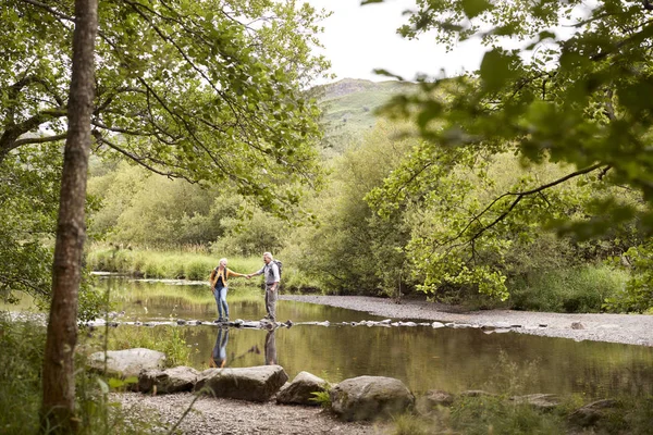 Senior Couple Crossing River Whilst Hiking Lake District — Stock Photo, Image