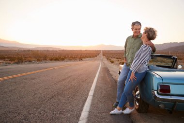 Senior couple on road trip standing by car, full length clipart