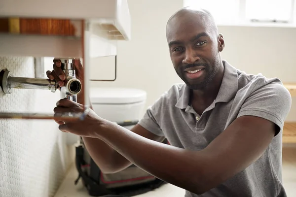 Young african man plumber sitting on floor and fixing a bathroom sink