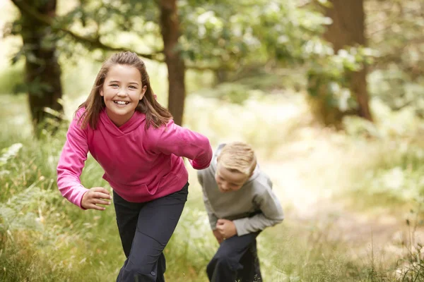 两个孩子走在森林中的绿地微笑着在相机 前面的视野 专注于前景 — 图库照片