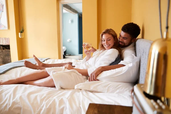 年轻的混血情侣在酒店床上喝饮料放松 — 图库照片