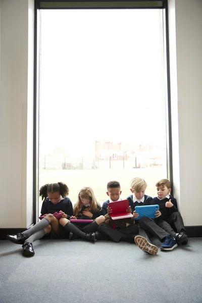 태블릿 컴퓨터를 사용하여 복도의 바닥에 줄지어 앉아있는 초등학교 아이들 — 스톡 사진
