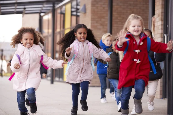 快乐的年轻女学生穿着外套 背着书包和同学在走道里跑 — 图库照片