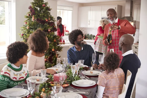 Чорний Дідусь Відкриває Шампанське Своєї Багатоповерхової Родини Зібравшись Їдальні Різдвяну — стокове фото