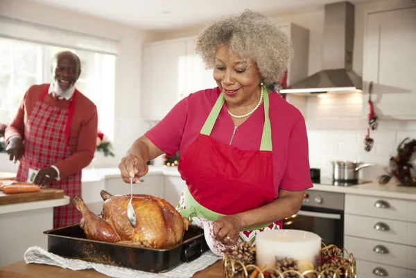 资深黑人女子为准备圣诞晚餐吃烤火鸡 丈夫在背景 正面看 — 图库照片
