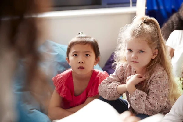 教室の快適なコーナーで豆袋の上に座っている2人の幼児の女の子は 彼らの先生に耳を傾ける — ストック写真