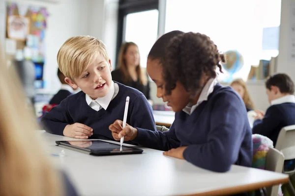 一个女孩和一个男孩使用平板电脑和手写笔坐在小学的课桌前 互相看着对方 — 图库照片