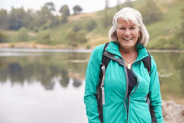Senior Caucasian woman standing on a shore of a lake smiling to camera, portrait