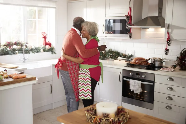 快乐的成熟的黑人夫妇拿着香槟眼镜 拥抱在厨房里 而准备在圣诞节早上的饭菜 侧视图 — 图库照片