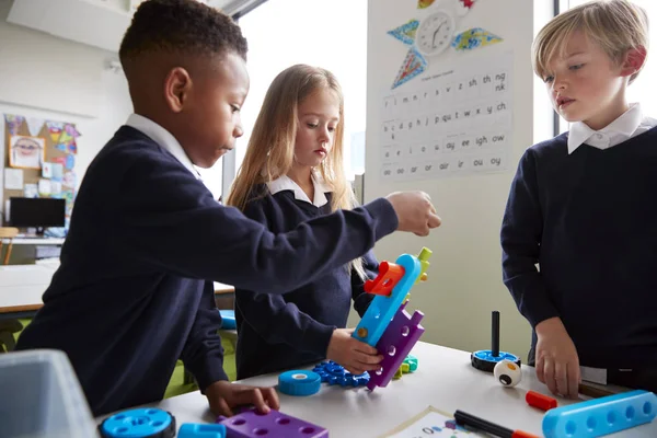 教室でおもちゃの建設ブロックと一緒に働く3人の小学生のクローズアップ 側面図 — ストック写真