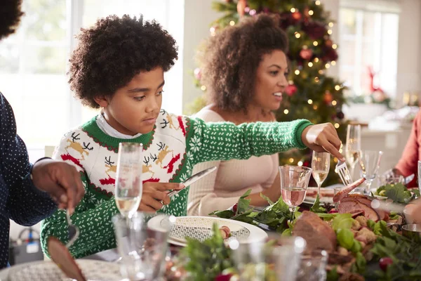 アフリカ系アメリカ人の少年が取り分けるローストターキー サイドビュー 家族でクリスマス ディナーのテーブルに座って — ストック写真