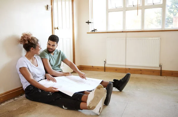 床に座ってカップルと新しい家の空の部屋で計画を見て — ストック写真
