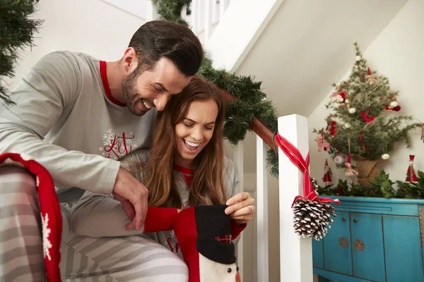 クリスマスの朝にストッキングを探して階段の上に座ってのパジャマを着て興奮しているカップル — ストック写真