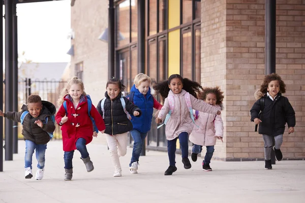 一群快乐的多民族小朋友穿着外套 背着书包在人行道上奔跑 — 图库照片