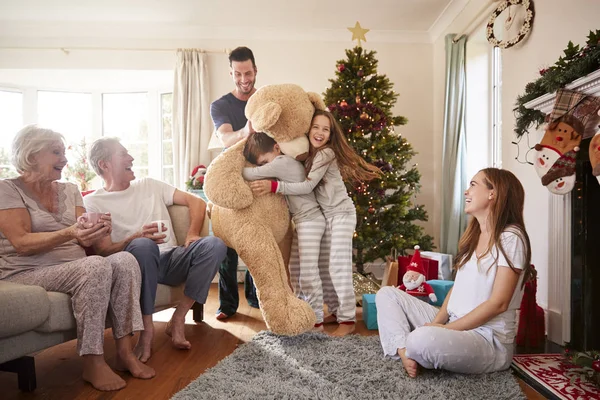 多世代家族として巨大なテディベアで遊んでいる子供たちにクリスマスの日に贈り物を開けない — ストック写真