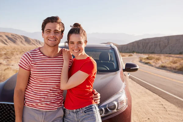 Young couple standing on desert roadside by car