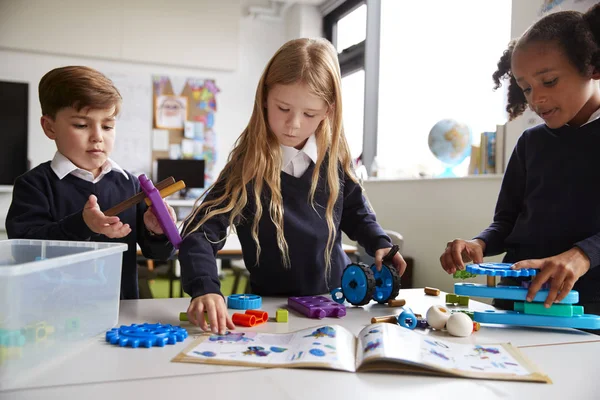 Drei Grundschulkinder Arbeiten Zusammen Folgen Einem Lehrbuch Und Verwenden Bausteine — Stockfoto