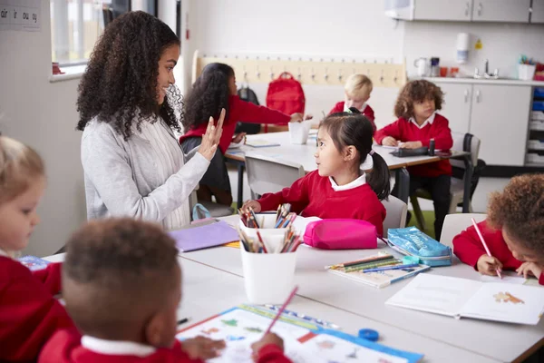 教室のテーブルに座る女子幼稚園教師が中国の若い女子高生に話し ジェスチャーをする 選択的な焦点 — ストック写真