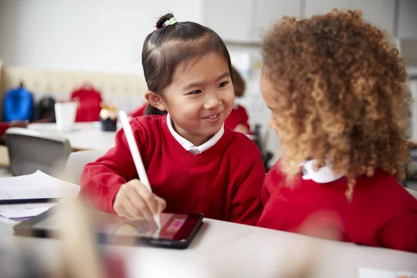 特写两名身着校服的幼儿园女学生 坐在教室的书桌旁 用平板电脑和手写笔 面带微笑地看着对方 — 图库照片