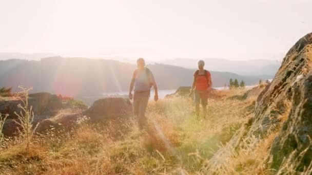 微笑的高级夫妇穿着背包爬山徒步穿越屋湖区与美丽的风景背景 拍摄慢镜头 — 图库视频影像