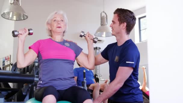 Seniorin Trainiert Fitnessstudio Auf Schweizer Ball Mit Handgewichten Und Wird — Stockvideo