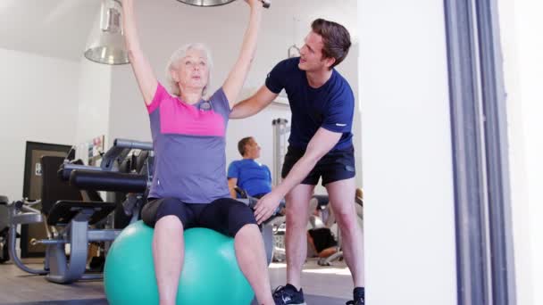 Senior Kvinna Utövar Schweizisk Boll Med Hand Vikter Gymmet Uppmuntras — Stockvideo