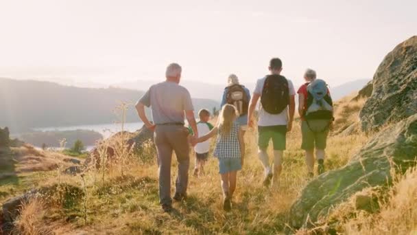 スローモーションで撮影で美しい風景を英国湖水地方でのハイキングにカメラから離れて歩いてバックパックを身に着けている多世代家族の後姿 — ストック動画