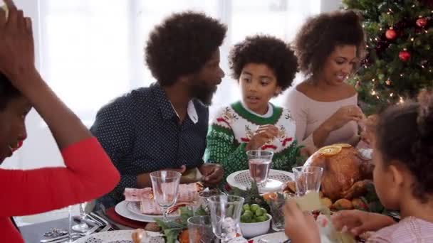 多世代混血家族紙の王冠を身に着けているクリスマスの夕食のテーブルに座っているショットをパン — ストック動画