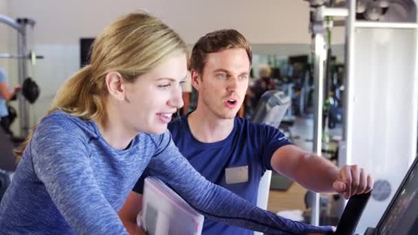Vrouw Trainen Fiets Machine Sportschool Wordt Aangemoedigd Door Mannelijke Personal — Stockvideo