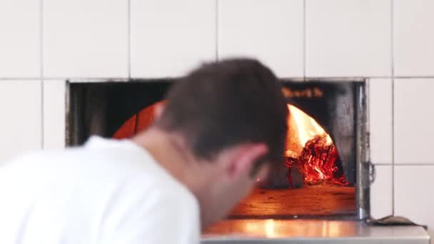 男は職人のパン屋で粘土オーブンで燃えている熱い石炭に薪の丸太を追加し クローズアップ — ストック動画