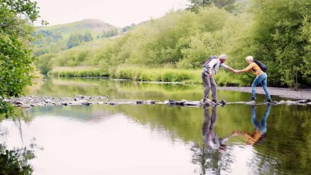 飛石で英国湖水地方 スローモーションで撮影を使用して川を渡る上級ハイキング カップルの全長側面図 — ストック動画