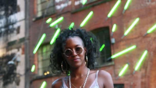 时尚的年轻黑人妇女在城市街道走到相机和焦点 低角度 模糊的霓虹灯背景 — 图库视频影像
