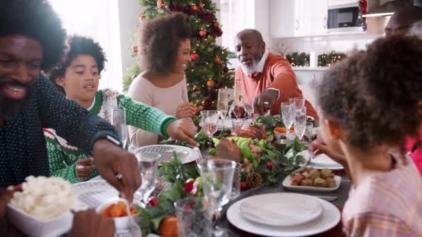 混合种族 多代家庭坐在他们的圣诞餐桌上 为自己提供食物和一起交谈 选择性的专注 — 图库视频影像