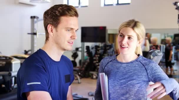 Man Exercising Cycling Machine Gym Being Encouraged Female Personal Trainer — Stock Video