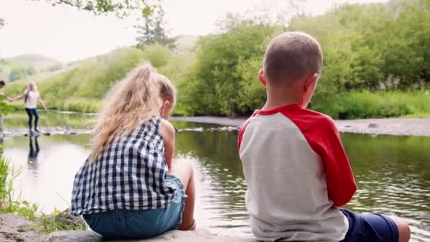 子供たちと湖の釣りの端によって岩の上に座っての背面ネットしながらバック グラウンドで スローモーションで撮影石のステップを使用して交差の両親 — ストック動画