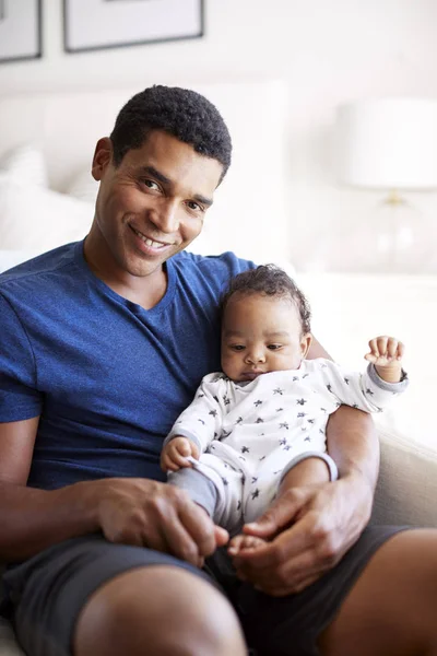 生後3ヶ月の赤ちゃんの息子を抱いて肘掛け椅子に座る若い大人の黒人の父親のクローズアップ カメラに微笑む — ストック写真
