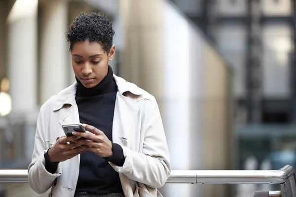 スマートフォンを使って街のビジネス街に立っている若い大人の女性は 前景に焦点を当てて — ストック写真