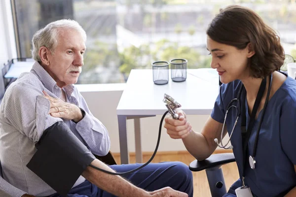 Pielęgniarka Noszenie Scrubs Biurze Sprawdzanie Starszy Mężczyzna Pacjentów Ciśnienie Krwi — Zdjęcie stockowe