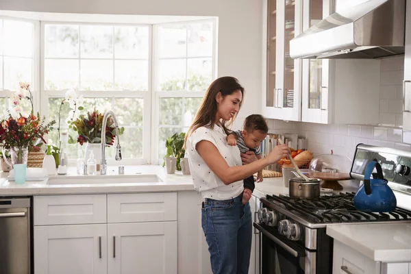 Multitarea Mamá Sosteniendo Bebé Mientras Hace Comida Cocina Vista Lateral —  Fotos de Stock