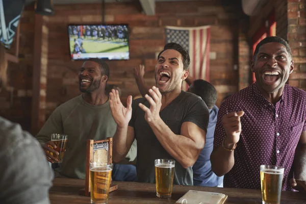スポーツバーで画面上のゲームを見ながら祝う男性の友人のグループ — ストック写真