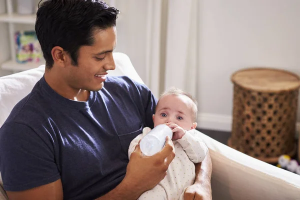 4ヶ月の息子を抱いて 自宅でボトルを与えるヒスパニック系の父親に笑顔 — ストック写真